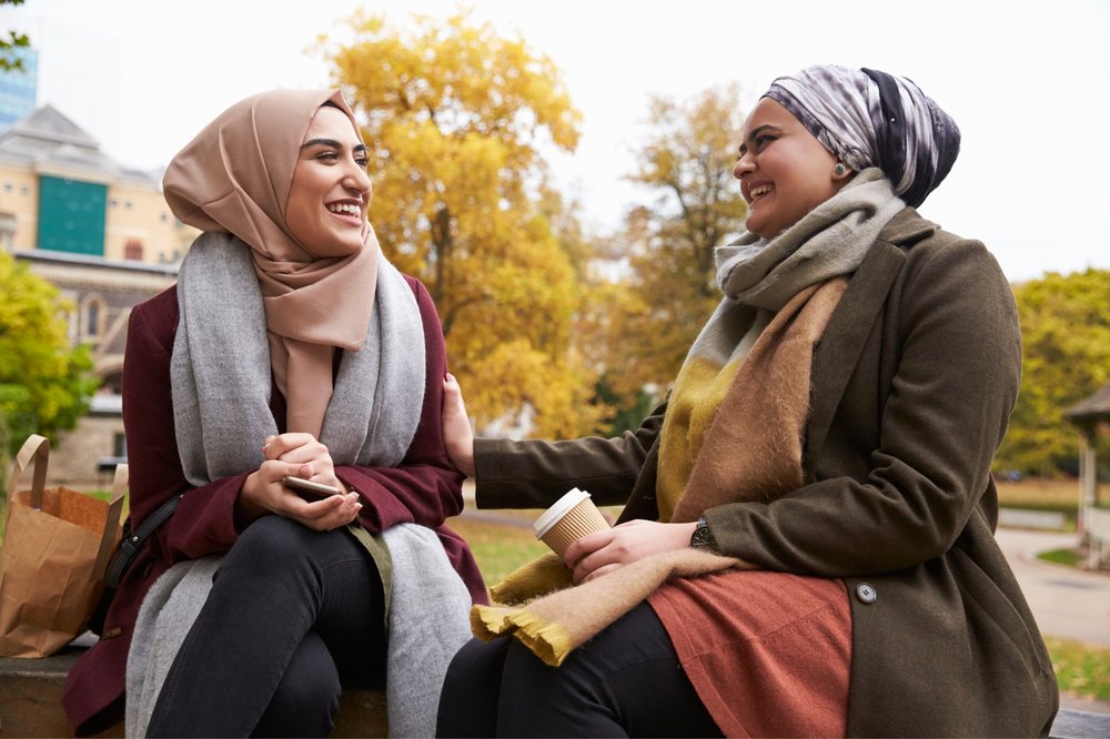 Two muslim women sitting in park laughing