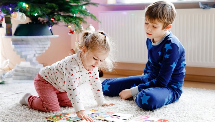 Two siblings, a little girl and boy, children sit on the floor at home playing together next to a decorated Christmas tree