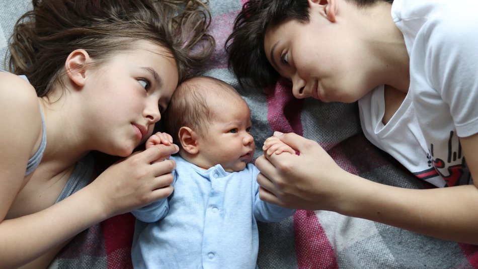 two siblings lying on a rug looking at their baby brother or sister