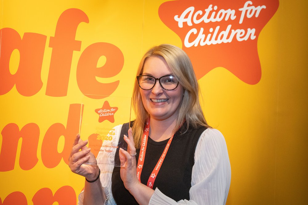 Woman holding up Stephenson Awards plaque in front of Action for Children banner