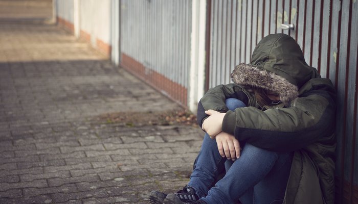 Worried looking child sitting on the floor against metal fence