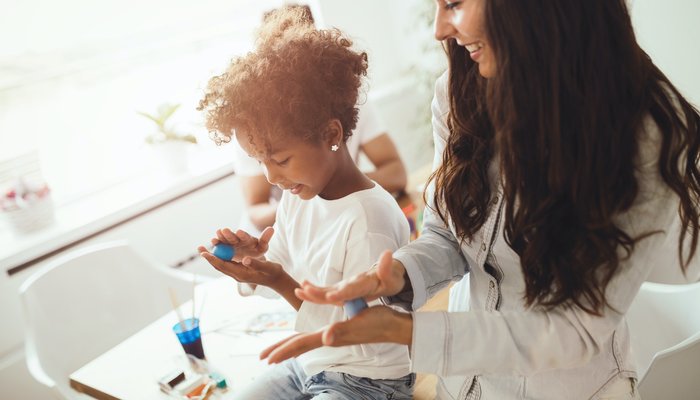 Young daughter and happy mother playing with play dough and smiling