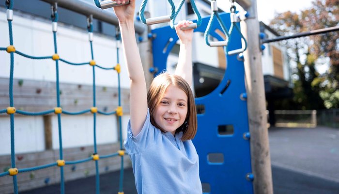 Young girl hanging from school playground monkey bars and smiling
