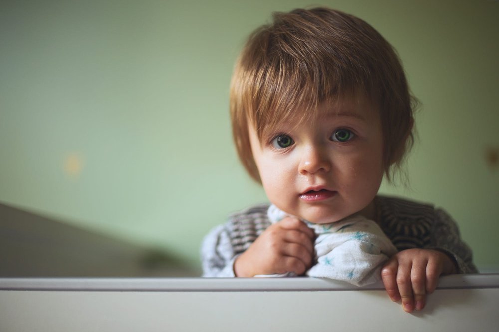 Young toddler leaning against cot with snuggly blanket