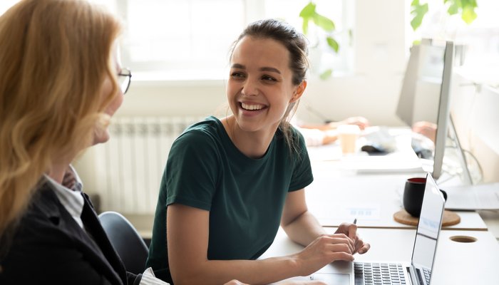 young woman sitting at desk smiling and tallkng to another women sat next to her