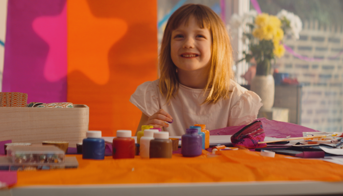 Abby, a young girl, looking up from her finger painting with a smile on her face