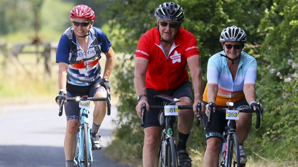 Three people on cycling. Person in the middle is wearing an Action for Children cycling t-shirt