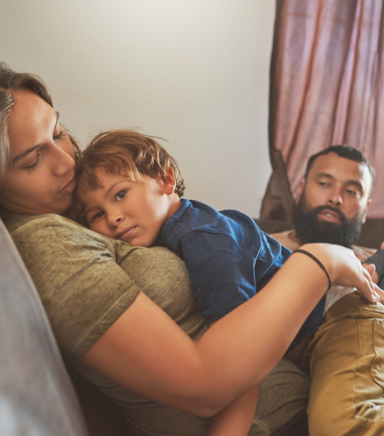 Little boy resting on his mother’s chest with his baby brother and father in the background